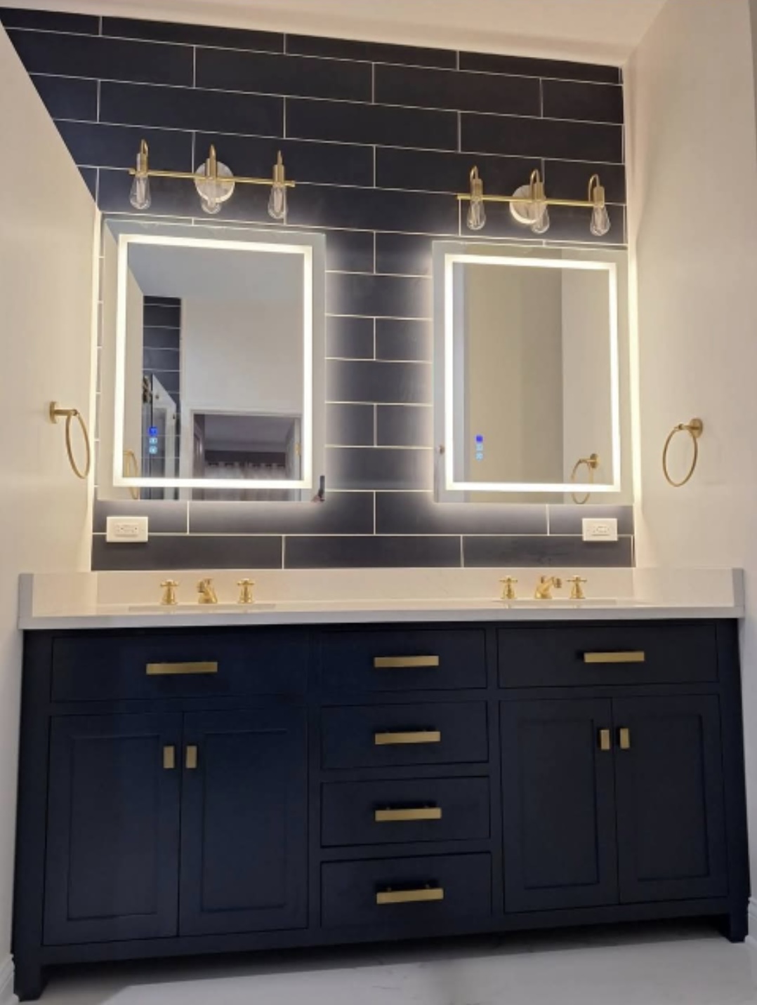 Remodeled bathroom with double vanity, backlit mirrors and black subway tile