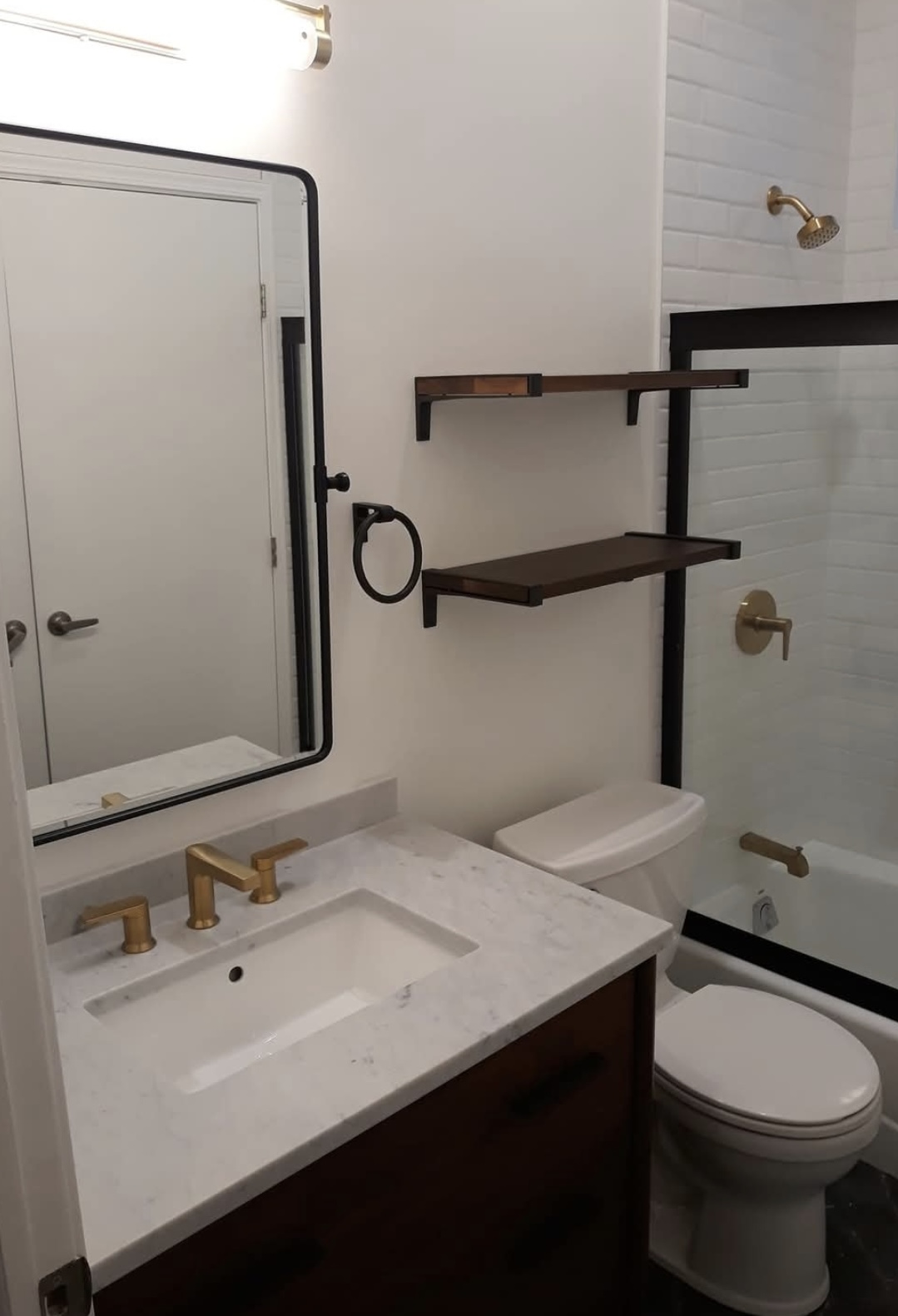 Bathroom with vanity, gold fixtures, floating wood shelves and glass shower
